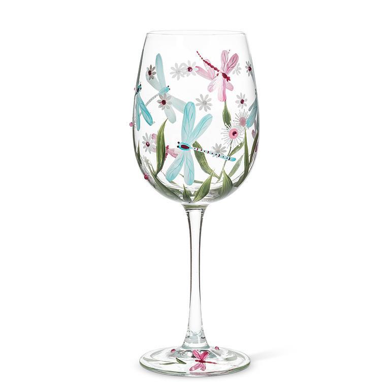 Verre à vin à pied transparent orné de motifs peints de libellules turquoise et roses, de feuillages verts et de petites fleurs délicates.
