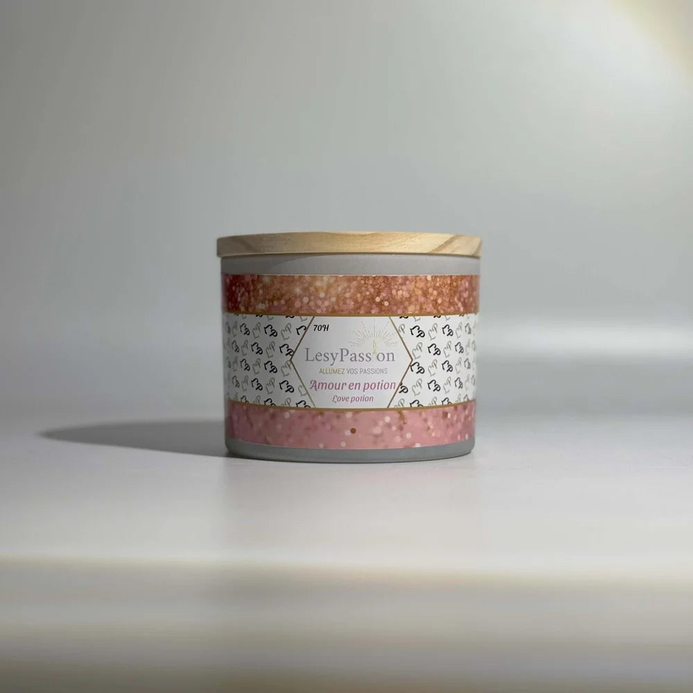 Bougie parfumée grand format 15 oz en pot large cylindrique avec couvercle en bois clair, arborant l'étiquette scintillante rose « Amour en potion / Love potion » de la marque LesyPassion sur fond épuré.