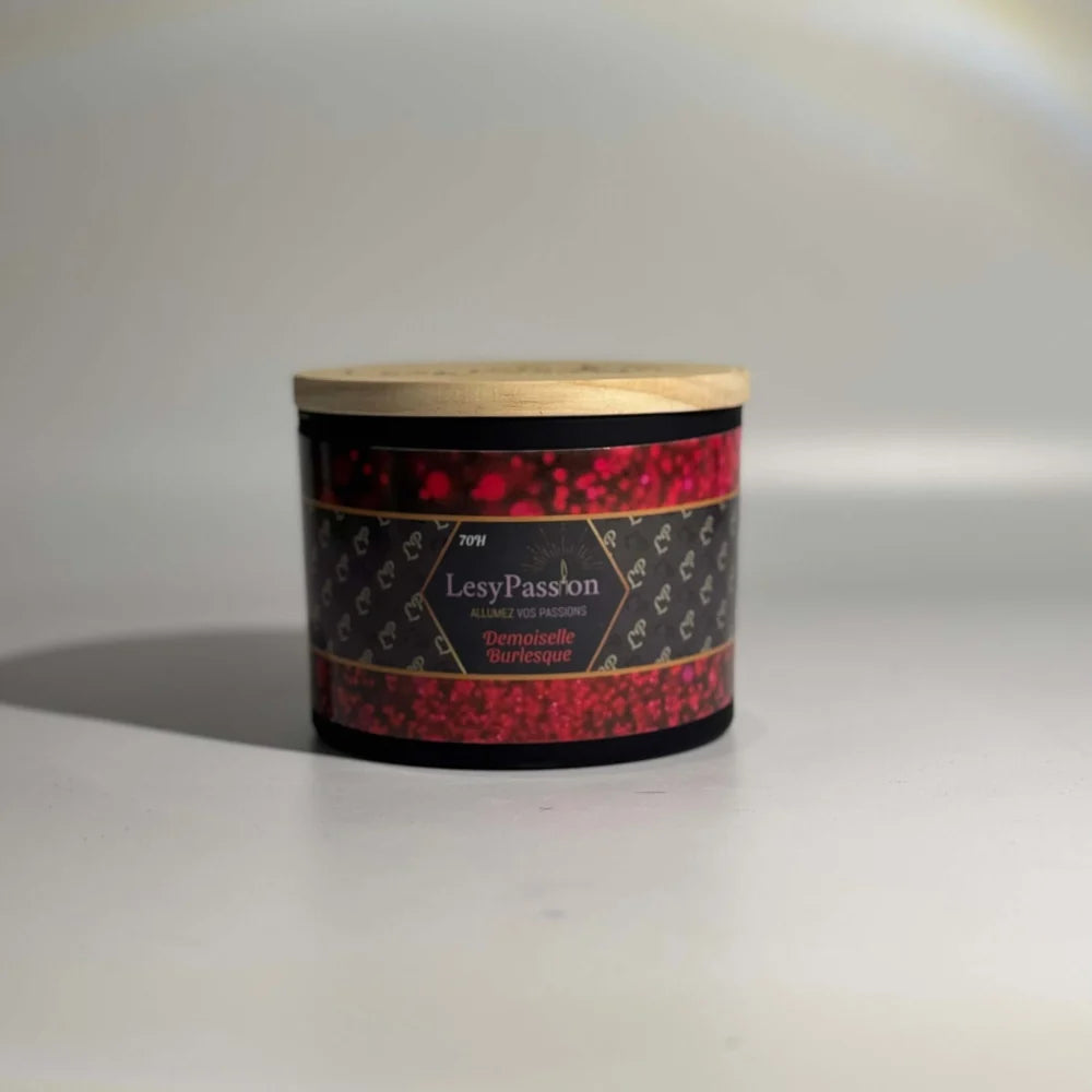 Bougie parfumée grand format 15 oz (70 h) en pot large noir mat avec couvercle en bois clair, arborant l'étiquette scintillante rouge « Demoiselle Burlesque » de la marque LesyPassion sur fond studio épuré.