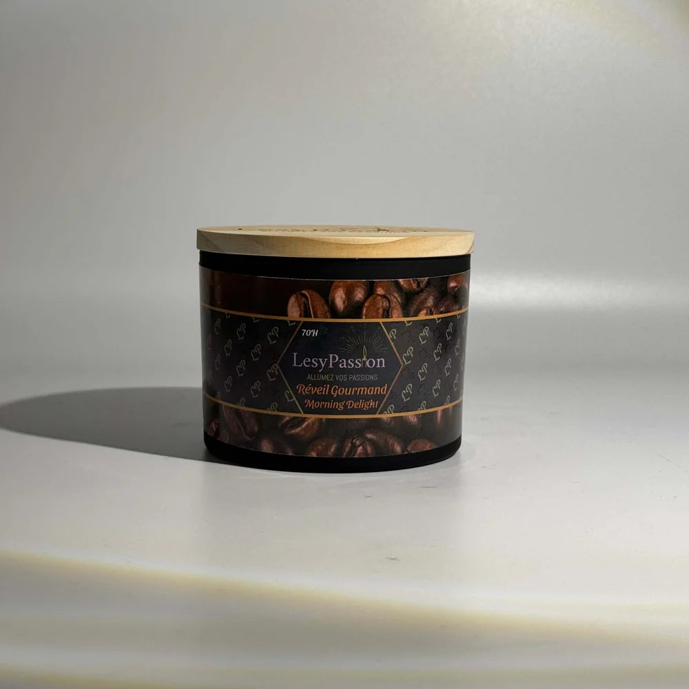 Bougie parfumée grand format 15 oz en pot large noir mat surmonté d'un couvercle en bois clair, arborant l'étiquette aux motifs de grains de café « Réveil Gourmand / Morning Delight » de la marque LesyPassion sur fond studio épuré.