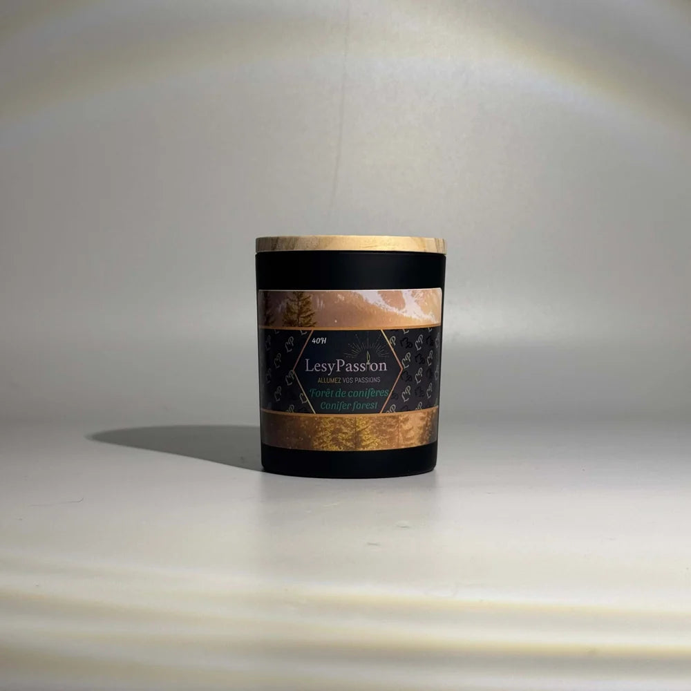 Bougie parfumée format moyen (40 h) en pot cylindrique noir mat avec couvercle en bois clair, arborant l'étiquette « Forêt de conifères / Conifer forest » de la marque LesyPassion sur fond studio épuré.
