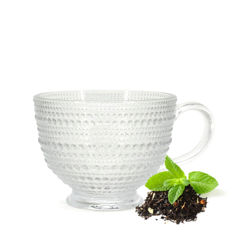 Tasse à thé en verre transparent texturé à motif perlé avec anse, présentée avec du thé en vrac et des feuilles de menthe fraîche