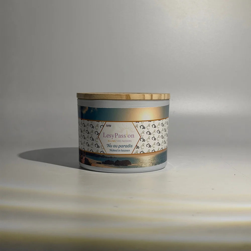 Bougie parfumée grand format 15 oz en pot large blanc surmonté d'un couvercle en bois clair, arborant l'étiquette « Nu au paradis / Naked in heaven » de la marque LesyPassion avec paysage marin au coucher du soleil.