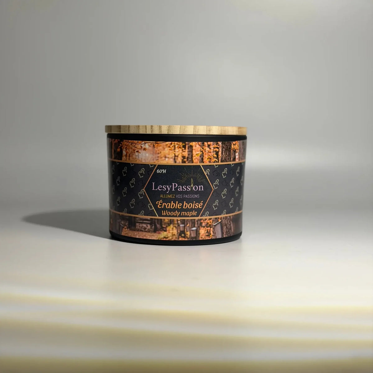 Bougie parfumée grand format (60 h) en pot large noir mat surmonté d'un couvercle en bois clair, dotée d'une étiquette « LesyPassion - Érable boisé / Woody maple » illustrée d'une érablière automnale, sur fond studio neutre. 