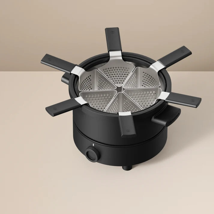 Appareil à fondue électrique noir compact (fondussimo )doté de six paniers perforés triangulaires vides, sur fond uni beige.
