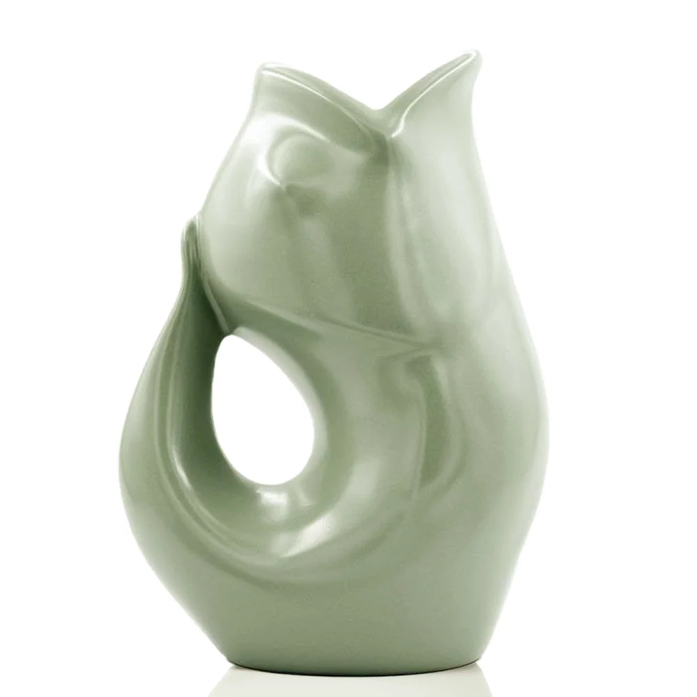 Carafe décorative (Gurgle Pot) en céramique émaillée de couleur vert sauge, sculptée en forme de poisson dressé dont la gueule ouverte sert de bec verseur et le corps courbé forme l'anse.