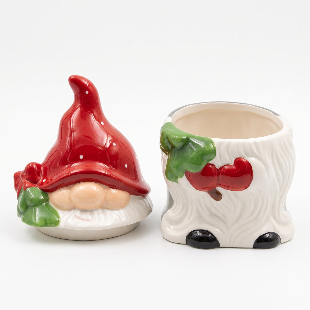 Jarre à biscuits en céramique en forme de gnome de Noël ouverte, montrant le couvercle à bonnet rouge posé à côté du pot intérieur vide sur fond blanc.