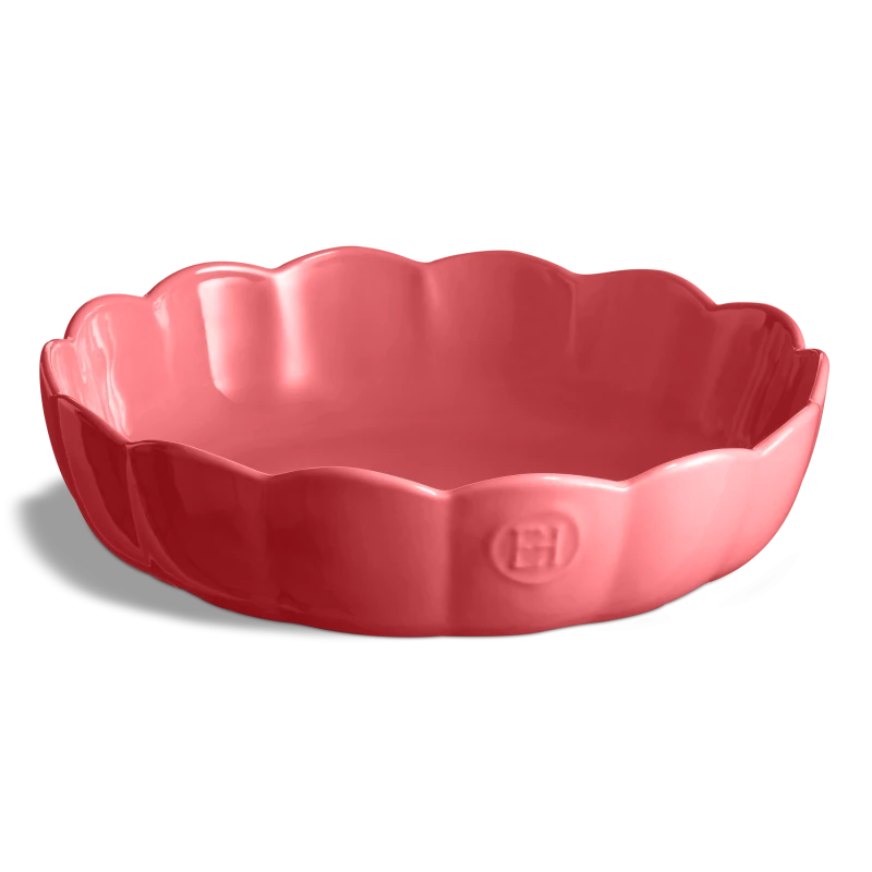Plat ou coupelle de service circulaire en céramique brillante de couleur rose. Les rebords sont ondulés et évasés en forme de corolle de fleur. Le sceau de la marque Emile Henry (« EH ») apparaît en relief sur la paroi extérieure avant. L'objet est présenté vide et centré sur un fond blanc neutre.