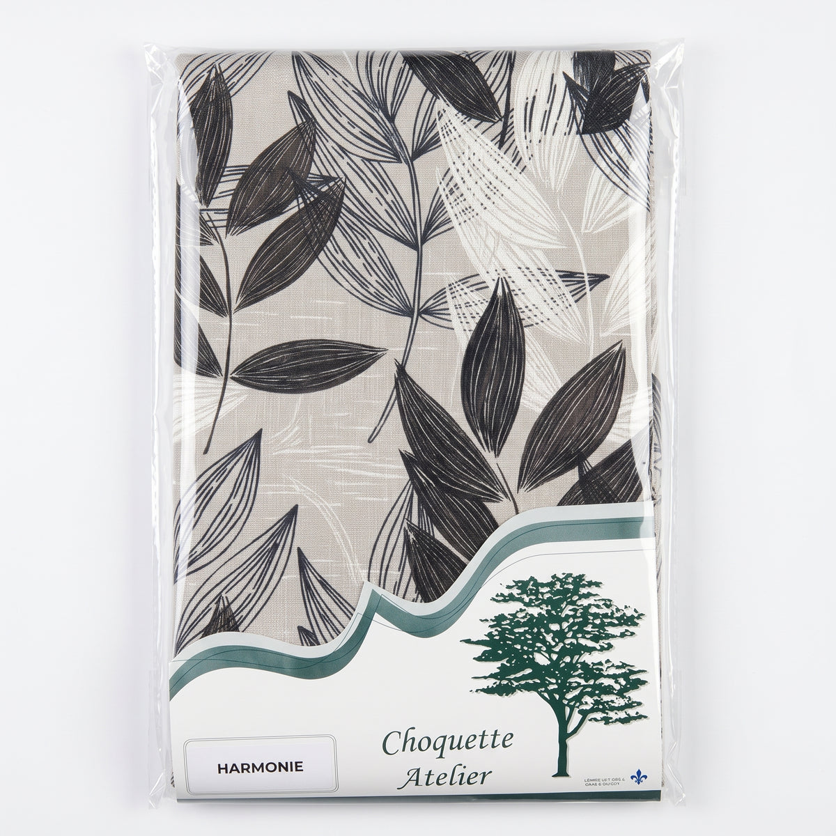Nappe pliée sous emballage plastique, marque Choquette Atelier, modèle Harmonie à motifs de feuillages graphiques noirs et blancs sur fond beige chiné.