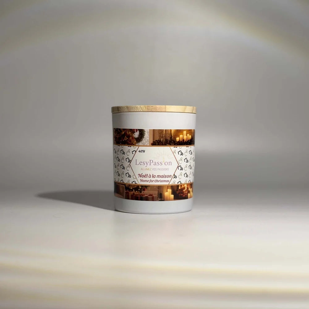 Bougie parfumée format moyen (40 h) en pot blanc cylindrique surmonté d'un couvercle en bois clair, arborant l'étiquette « Noël à la maison » de la marque LesyPassion sur fond studio épuré.