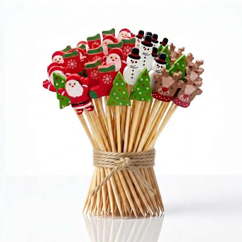 Bouquet de bâtonnets décoratifs et cure-dents en bois pour bouchées festives, ornés de figurines de Noël colorées (Pères Noël, sapins, bonhommes de neige, bas de Noël et rennes), attachés par une ficelle de jute sur fond blanc